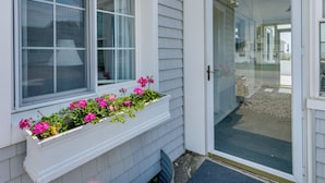 A house with a white exterior, a glass door, and a window with a flower box. - Cozy Westbrook Vacation Rental - Walk to Beach! (Westbrook)