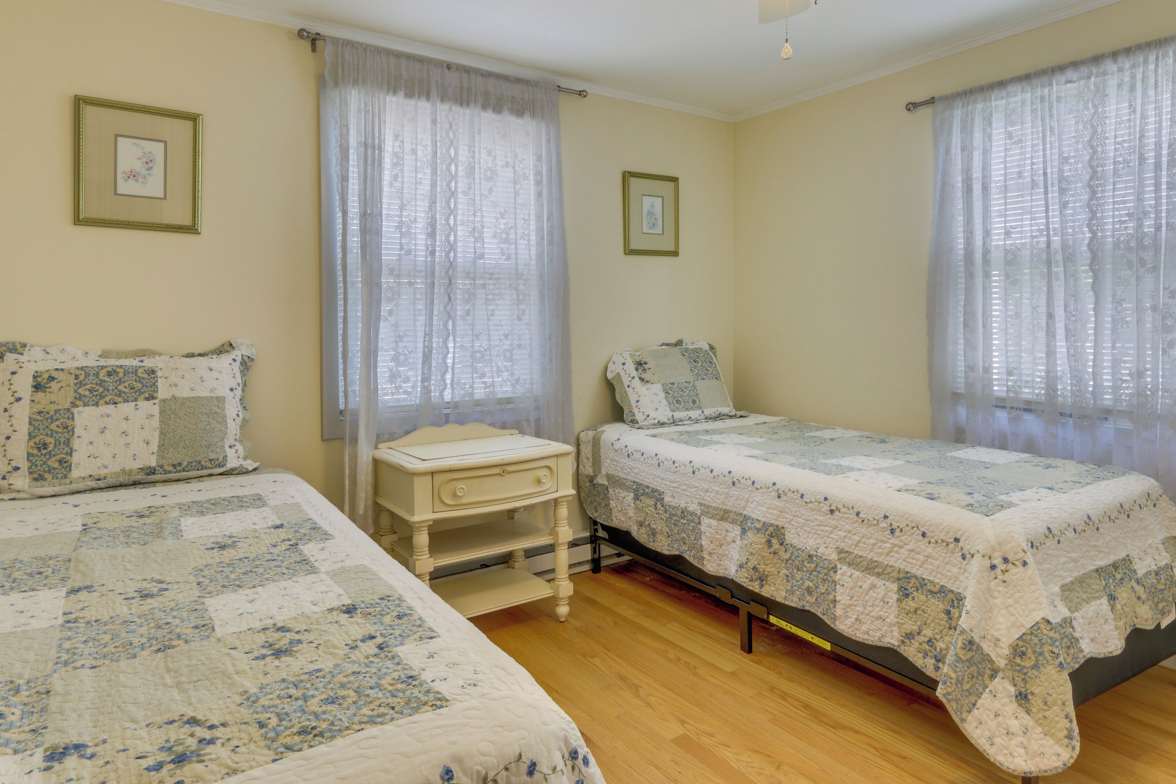 Una habitación con dos camas, una mesita de noche y un ventanal con cortinas traslúcidas.