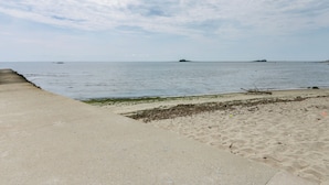A beach with a concrete walkway, sandy shore, and calm sea. - Cozy Westbrook Vacation Rental - Walk to Beach! (Westbrook)