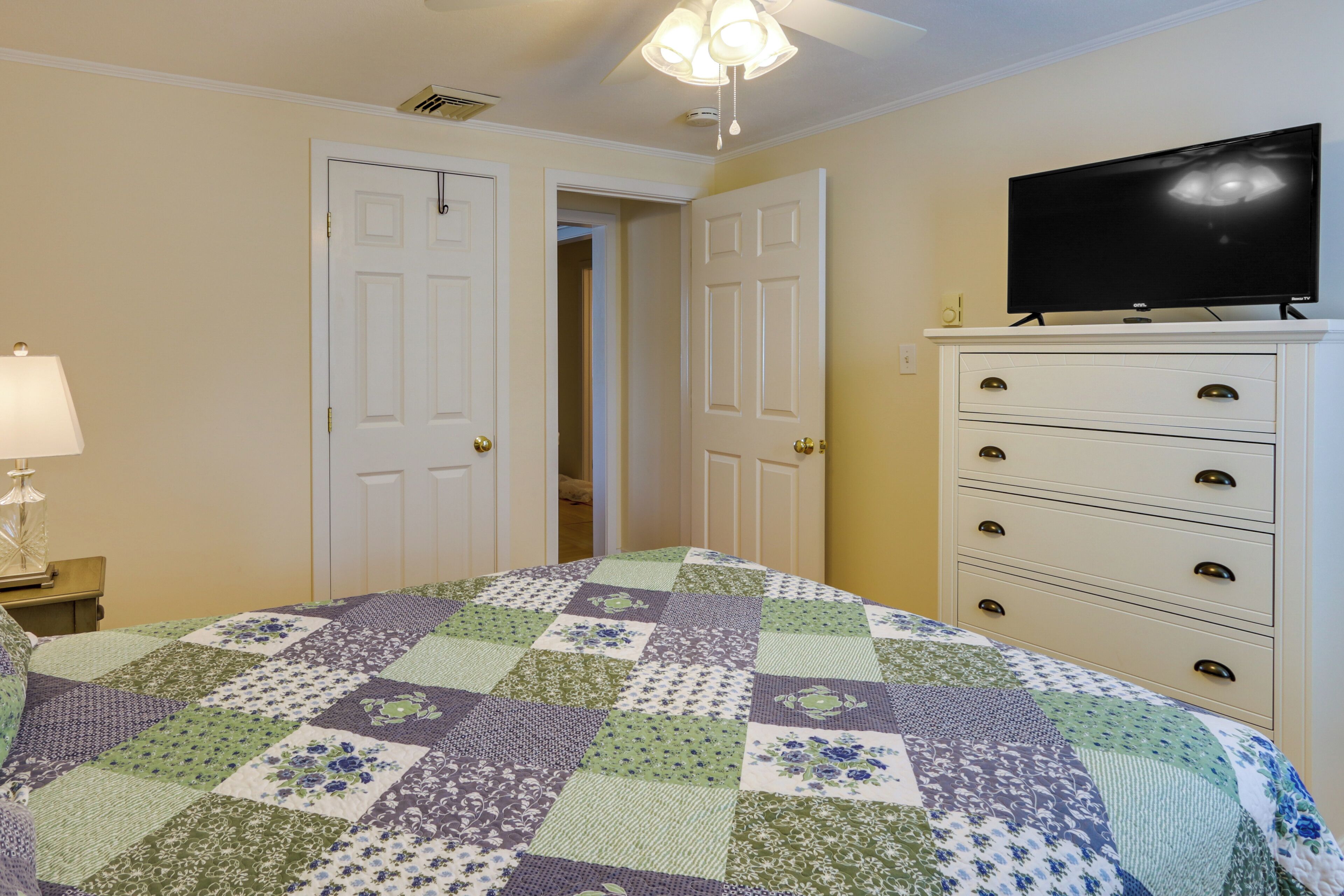 Une chambre à coucher comprenant un lit, une commode, un téléviseur et deux portes donnant sur d’autres pièces.