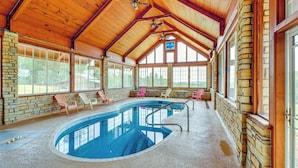 Una grande piscina interna con soffitto in legno e pareti in pietra, circondata da sedie a sdraio e tavolini.