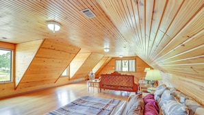 Una stanza con soffitto alto e travi in legno, un letto con coperta a righe, una panca di legno e un tavolo con una lampada.