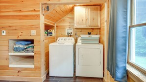 A compact laundry room with wooden walls, a washing machine, a dryer, and a shelf with folded clothes. - Meredith Home w/ Deck: 6 Mi to Lake Winnipesaukee! (Meredith)