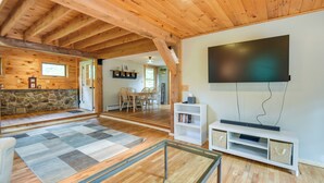 A spacious living area with wooden floors, a large flat-screen TV mounted on the wall, a stone accent wall, and a dining area in the background. - Meredith Home w/ Deck: 6 Mi to Lake Winnipesaukee! (Meredith)