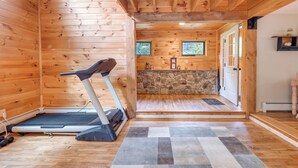 A wooden cabin interior with a treadmill, a stone fireplace, and a small kitchen area. - Meredith Home w/ Deck: 6 Mi to Lake Winnipesaukee! (Meredith)
