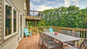 A wooden deck with a table and chairs, a small balcony, and a view of trees. - Meredith Home w/ Deck: 6 Mi to Lake Winnipesaukee! (Meredith)