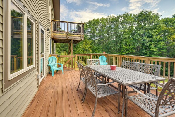 A wooden deck with a table and chairs, a small balcony, and a view of trees.