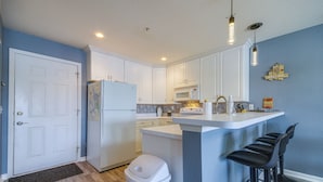 A modern kitchen with white cabinets, a central island with bar stools, a microwave, and a refrigerator.