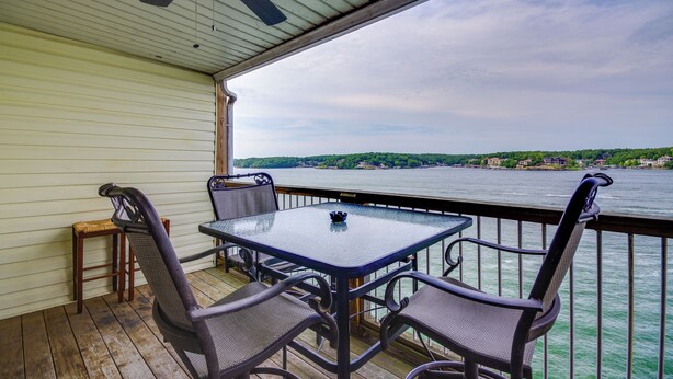 A covered deck with a table and chairs, overlooking a body of water with a distant shoreline.