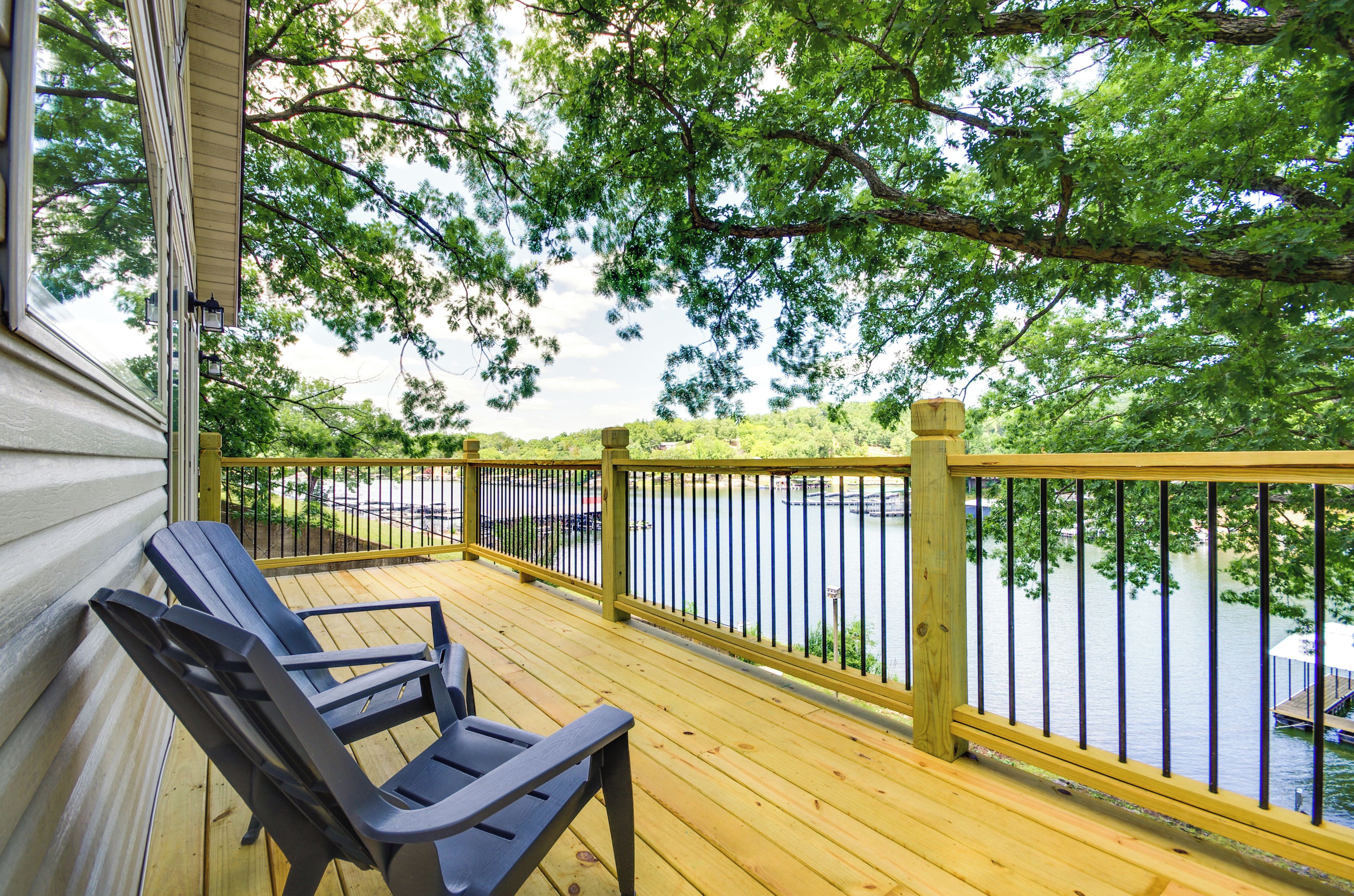 A wooden deck with a railing overlooking a body of water, a bench, and a view of trees and a dock.