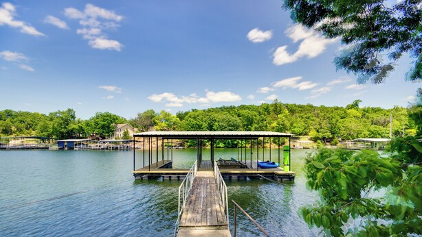 A wooden dock leading to a covered boat launch area with a calm lake and lush greenery in the background.
