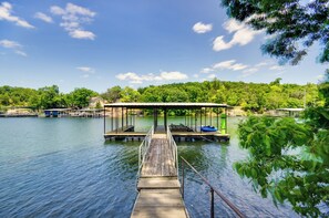 A wooden dock leading to a covered boat launch area with a calm lake and lush greenery in the background.