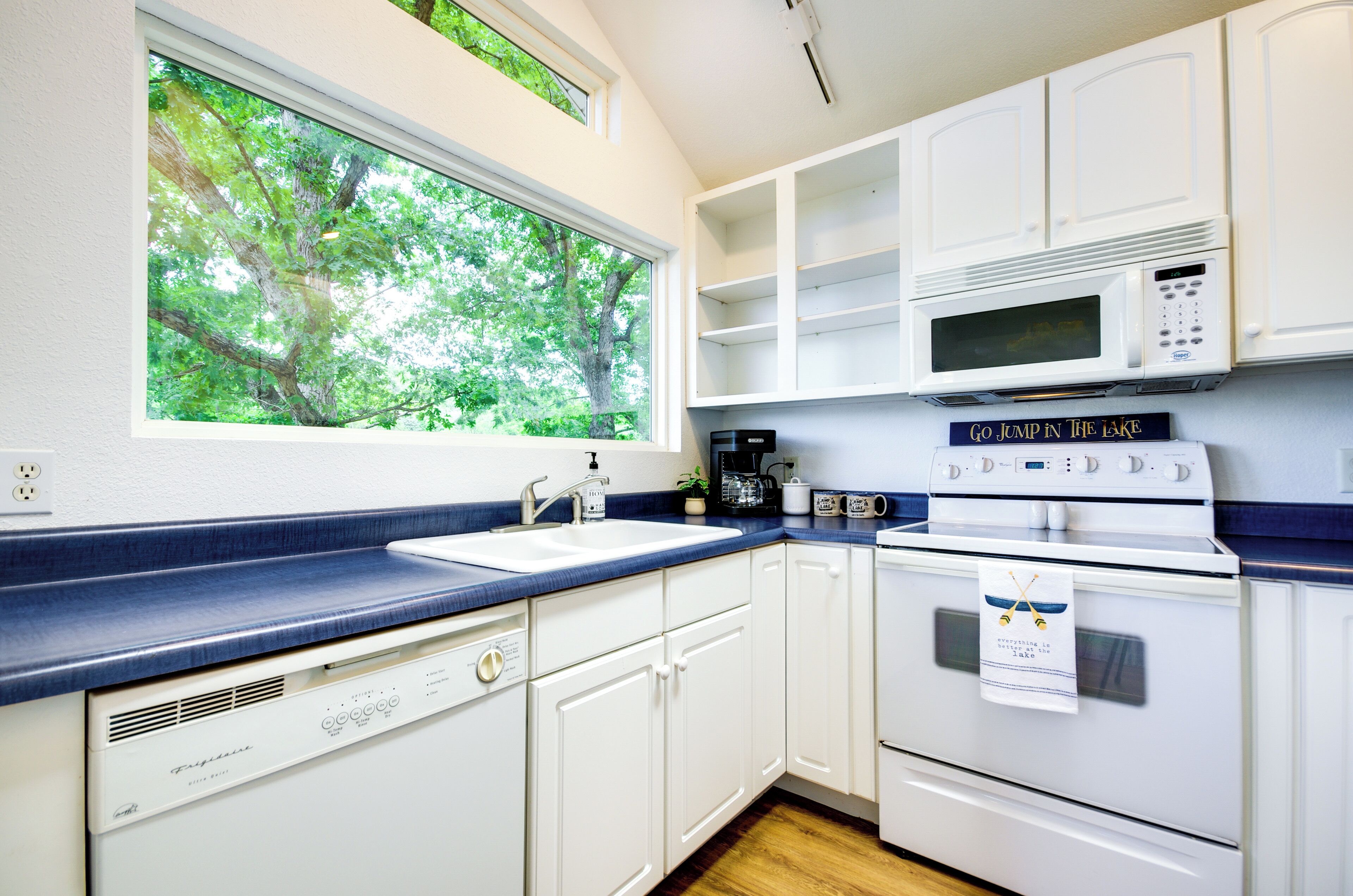 A kitchen with white cabinets, a blue countertop, a window with a view of trees, a microwave, and a stove.