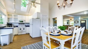 A modern kitchen with white cabinets, a microwave, and a refrigerator. There is a dining area with a wooden table and white chairs.