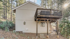 A cabin with a wooden deck and a large window, surrounded by trees. - Deck & Gas Grill: Secluded Arnold Cabin Rental! (Arnold)