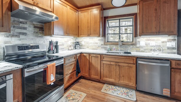 A modern kitchen with wooden cabinets, a stainless steel range hood, a dishwasher, and a window providing natural light. - Deck & Gas Grill: Secluded Arnold Cabin Rental! (Arnold)