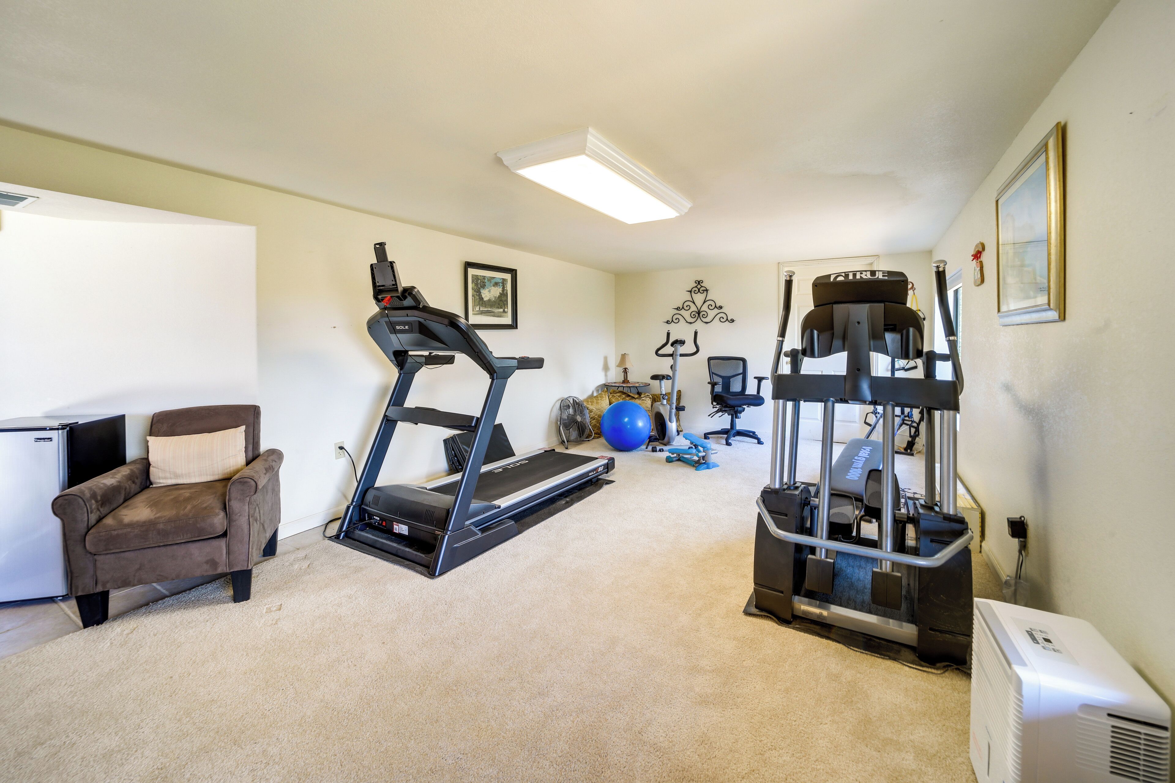 A home gym with a treadmill, exercise ball, and weight machine.