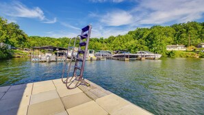 A dock with a chair and a boat, surrounded by water and greenery. - Lakefront Osage Beach Retreat w/ Boat Slip! (Osage Beach)