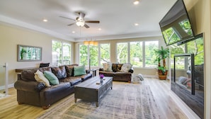 A spacious living room with a ceiling fan, large windows, and a flat-screen TV mounted on the wall. - Lakefront Osage Beach Retreat w/ Boat Slip! (Osage Beach)