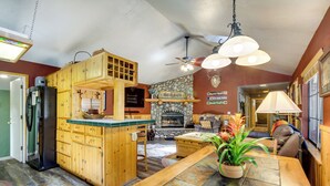 A cozy interior with a stone fireplace, wooden cabinetry, and a dining area with a table and chairs. - Central Big Bear Lake Retreat w/ Private Hot Tub! (Big Bear Lake)