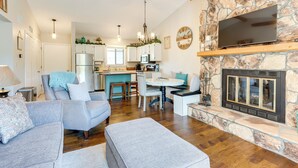 Una sala moderna con chimenea de piedra, un comedor y una cocina con armarios blancos y una pared de acento de piedra.