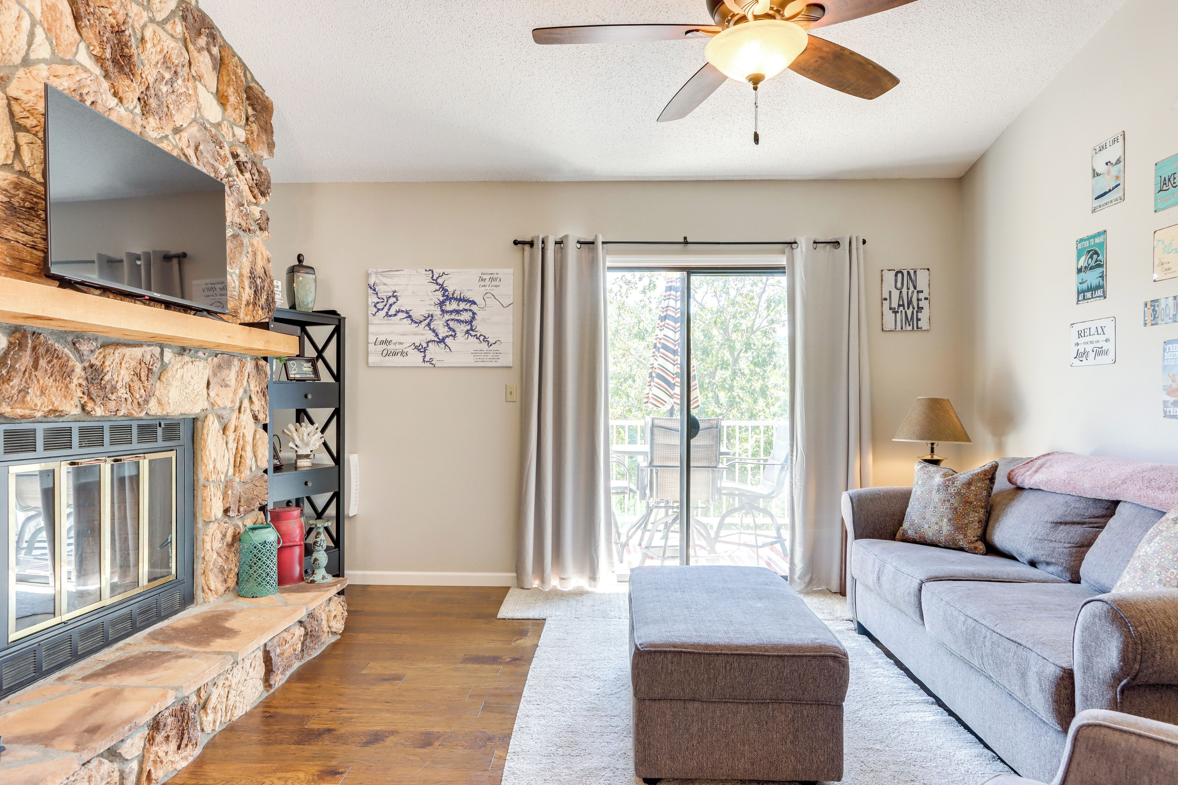 A living room with a stone fireplace, a ceiling fan, a couch, and a sliding glass door leading to an outdoor patio.