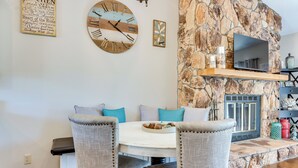 Un comedor con pared de piedra, un reloj de pared y un televisor de pantalla plana sobre una estantería.