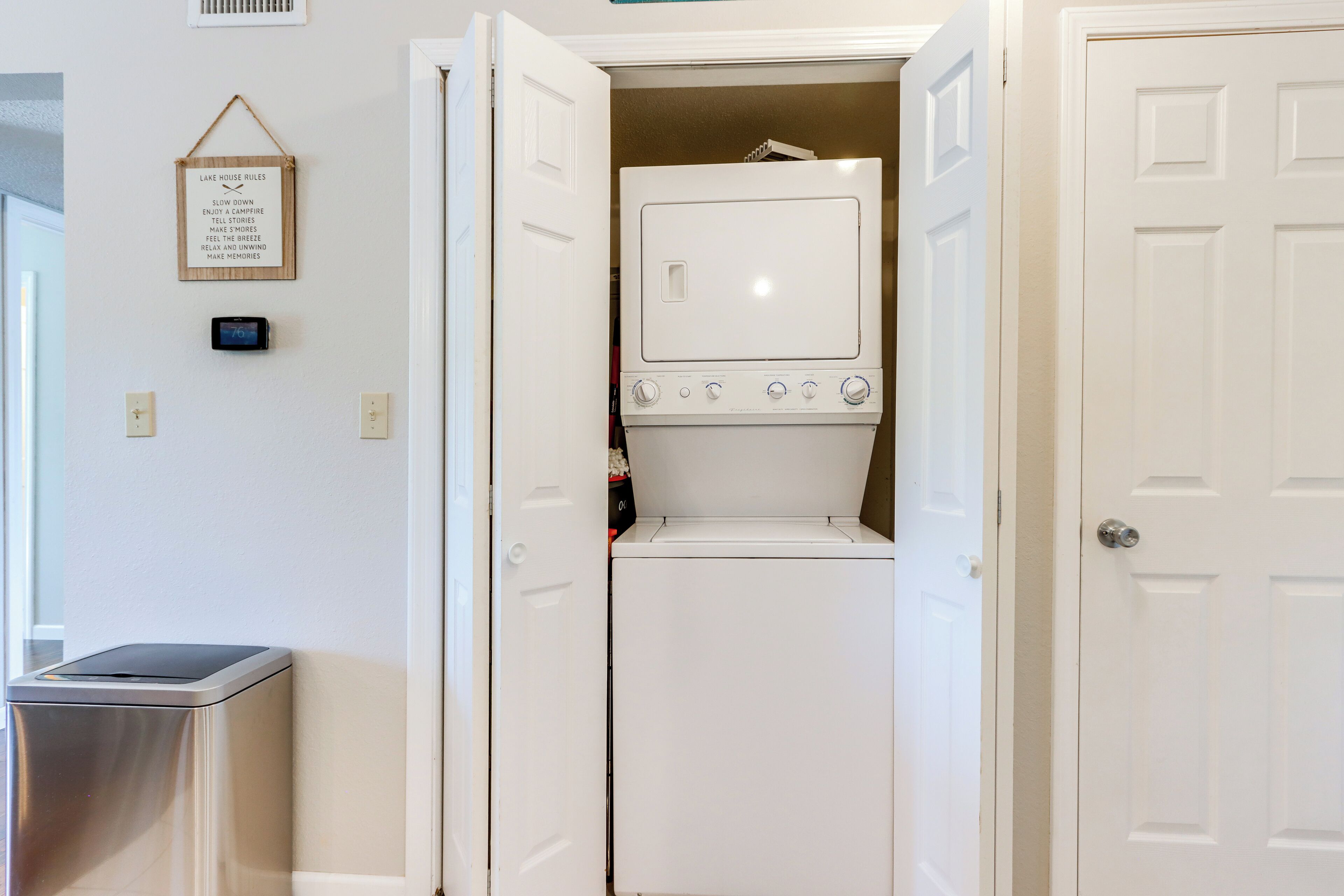 A laundry room with a washing machine and dryer, a trash can, and a wall-mounted thermostat.