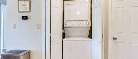 A laundry room with a washing machine and dryer, a trash can, and a wall-mounted thermostat.
