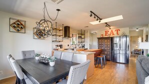 Une cuisine moderne dotée d’un îlot central, d’appareils électroménagers intégrés et d’un coin repas avec une table en bois foncé et des chaises rembourrées.