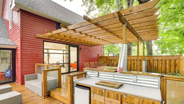 Eine Holzterrasse mit Pergola, Gartenmöbeln und einem kleinen Kühlschrank.