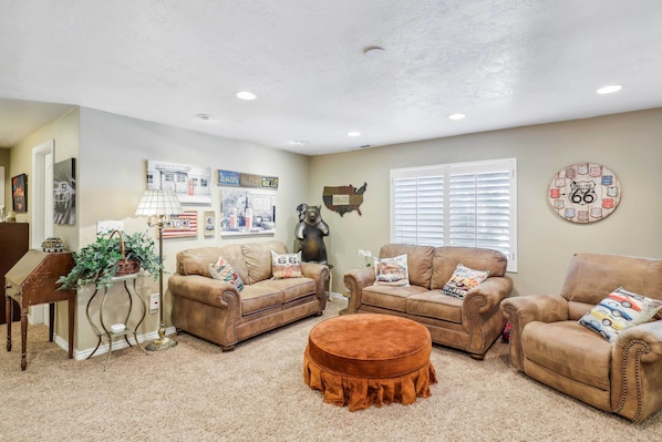 A living room with two brown leather sofas, a round ottoman, a small wooden table with a plant, and wall decorations including a map and Route 66 signs. - Secret Garden Retreat Private Patio Kitchen (American Fork)