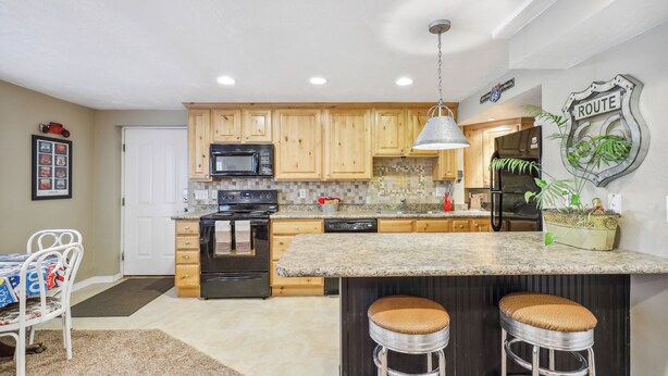 A kitchen with wooden cabinets, a granite countertop, a stainless steel refrigerator, and a bar stool.