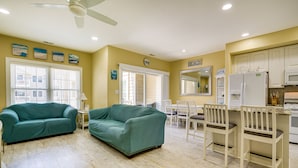 A spacious living room with two green sofas, a dining area with white chairs, and a kitchen with white cabinets and appliances. - North Wildwood Townhome < 1/2 Mi to Beach! (North Wildwood)