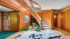 Un escalier en bois orné d’un lustre, un tapis en peau de vache et un petit coin jardin avec des plantes.