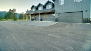 A large, two-story building with a garage, a covered porch, and a gravel driveway. - Modern Donnelly Cabin w/ Private Hot Tub (Donnelly)
