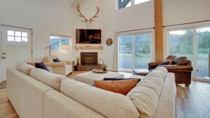 A spacious living room with a large sofa, a fireplace, and a television mounted on the wall. - Modern Donnelly Cabin w/ Private Hot Tub (Donnelly)