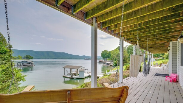 A wooden swing chair on a covered deck overlooking a lake with boats and docks. - Waterfront Smith Mountain Lake Home w/ Dock! (Huddleston)