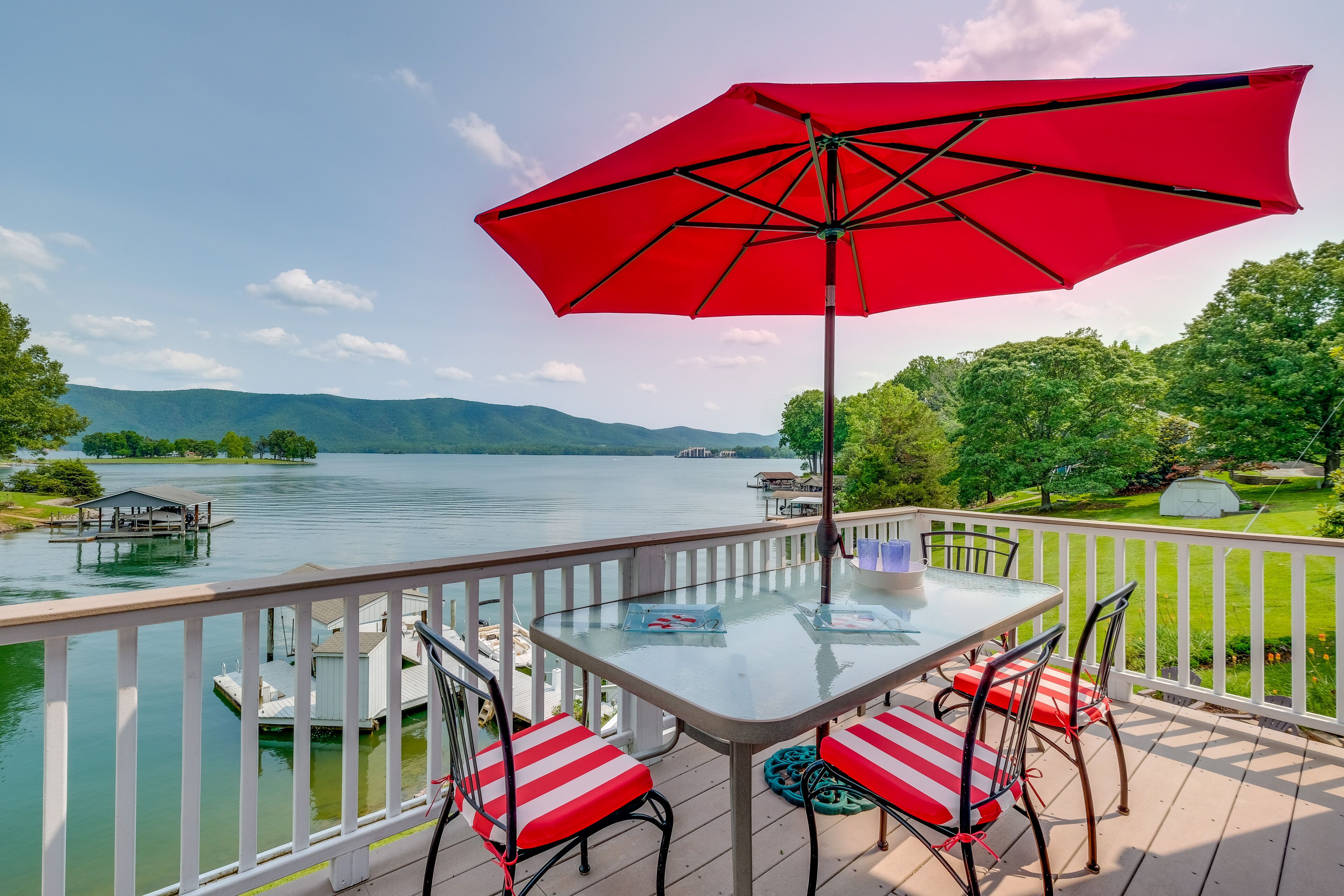 Une terrasse avec une table en verre, des chaises à rayures rouges et blanches et un parasol rouge.