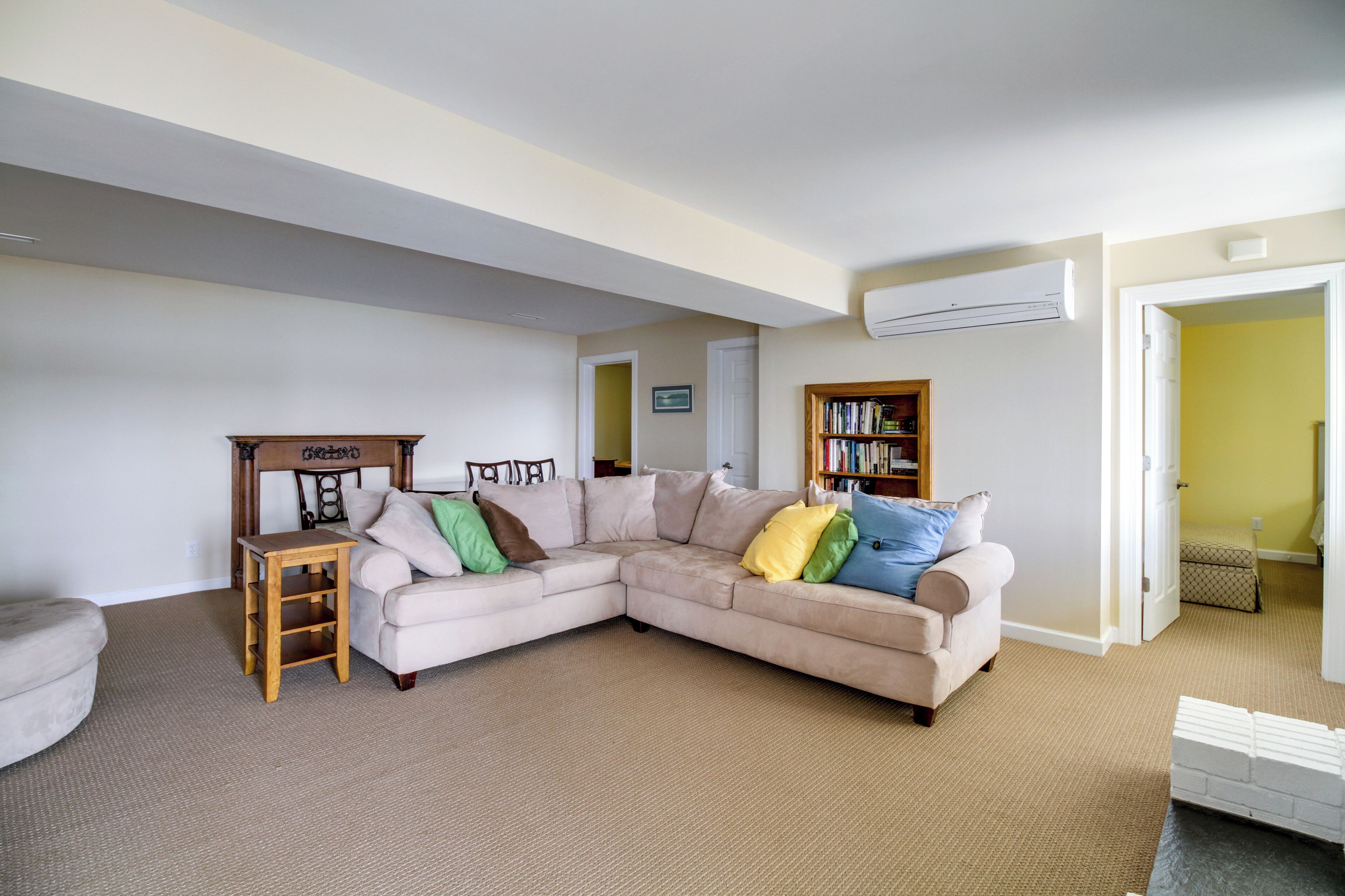 A living room with a beige sectional sofa, a wooden side table, and a bookshelf.