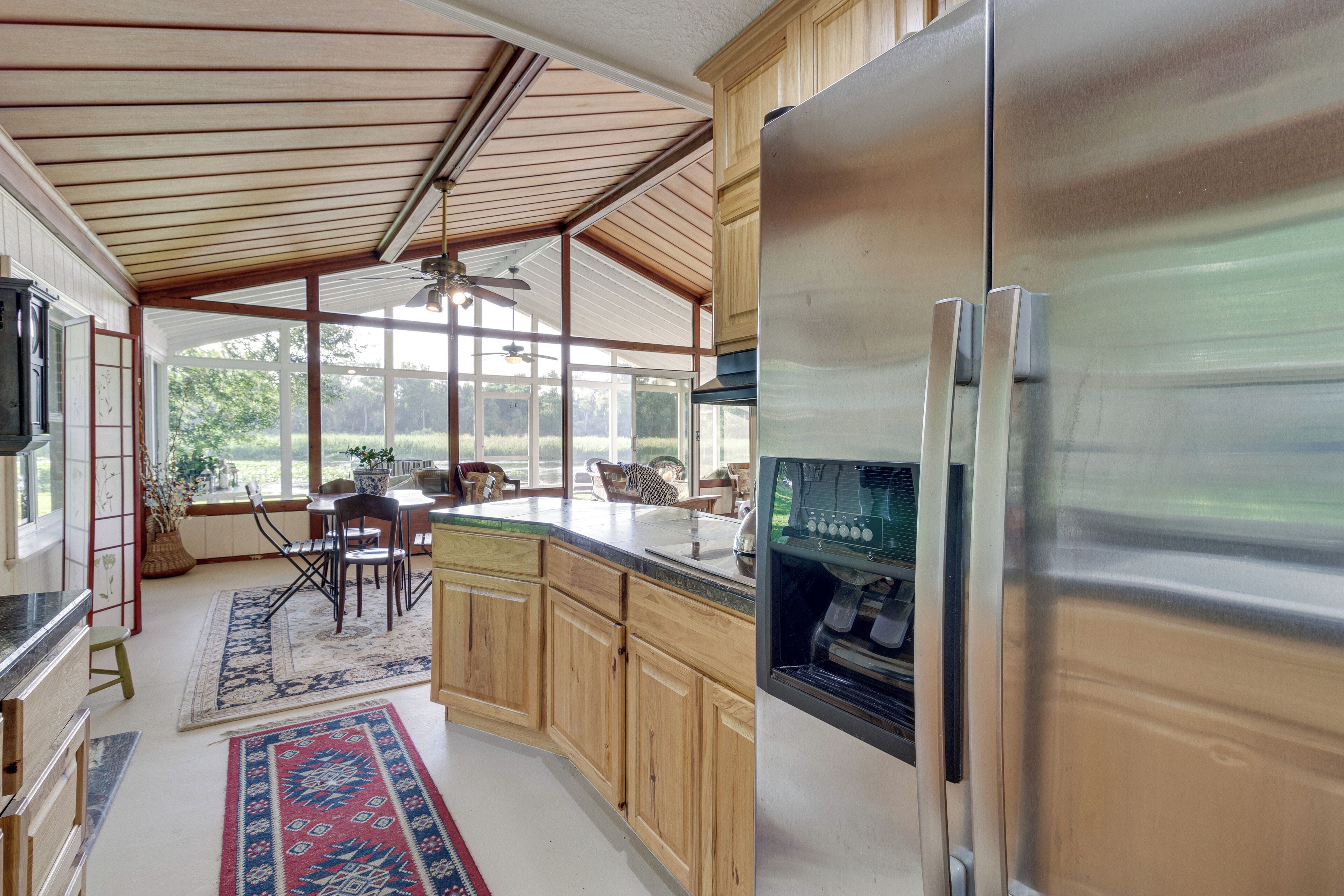A kitchen with wooden cabinets, a stainless steel refrigerator, and a large window overlooking a garden.