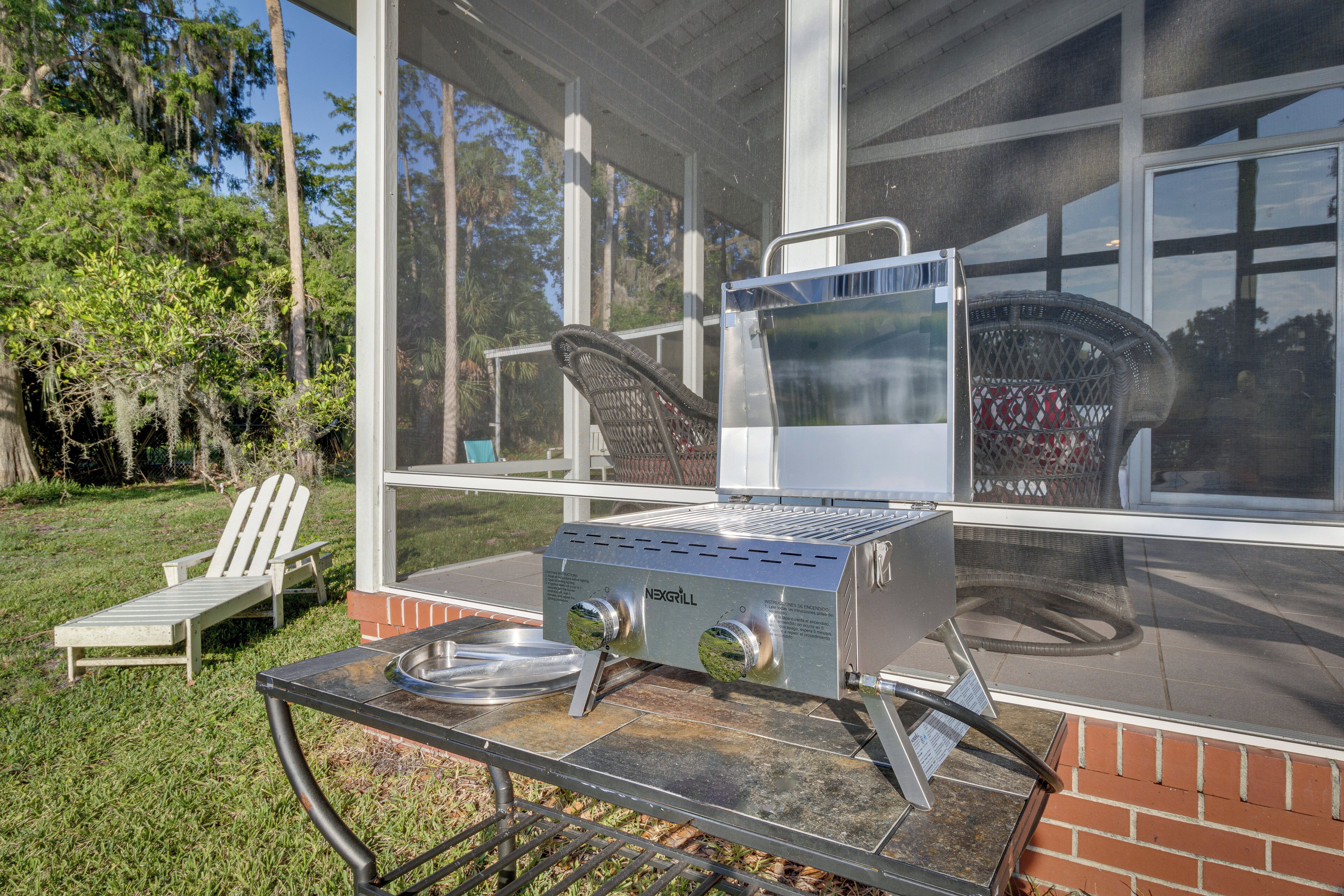 A patio with a grill, a chair, and a view of a house through a window.
