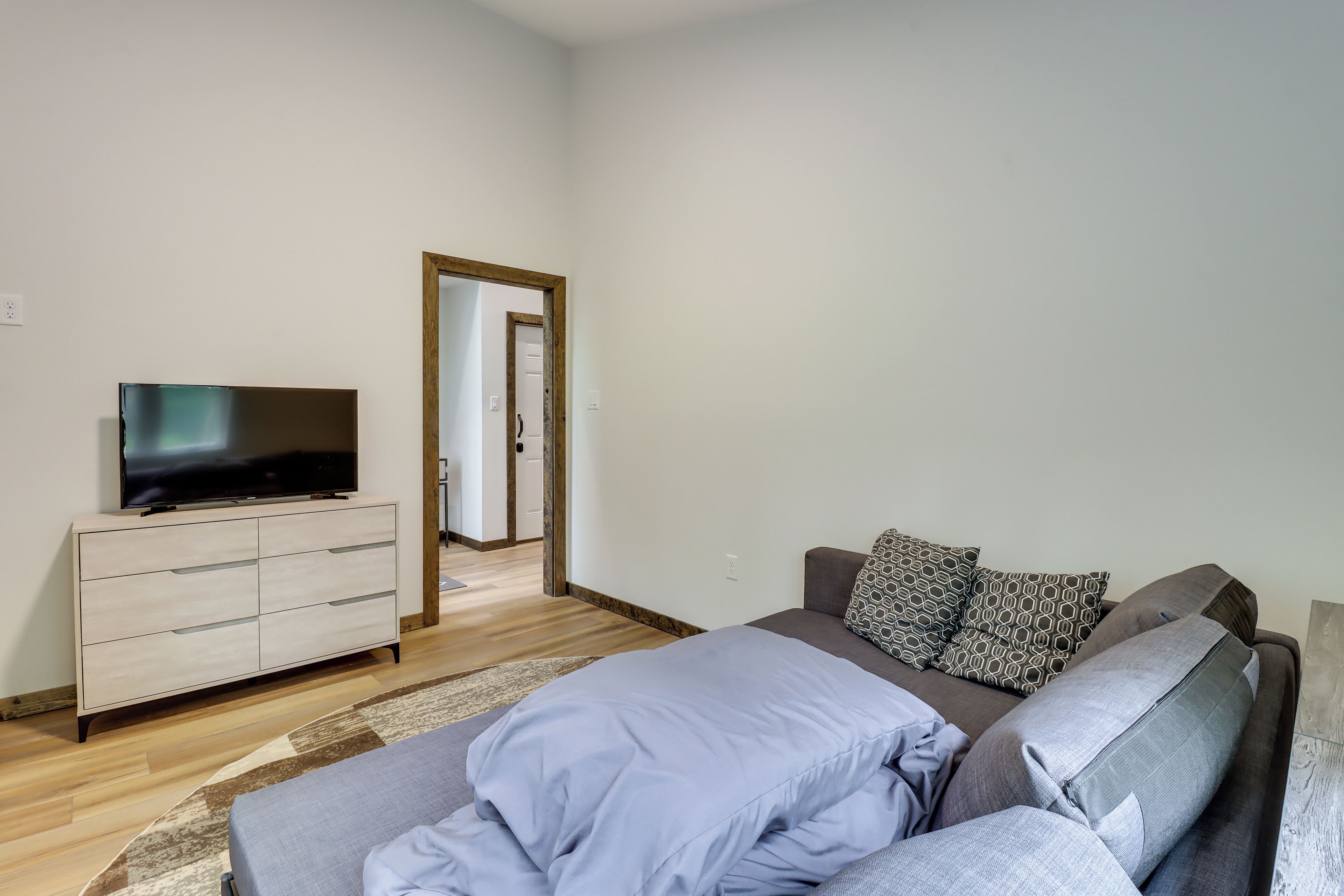 A modern bedroom with a bed, a TV on a dresser, and a door leading to another room.