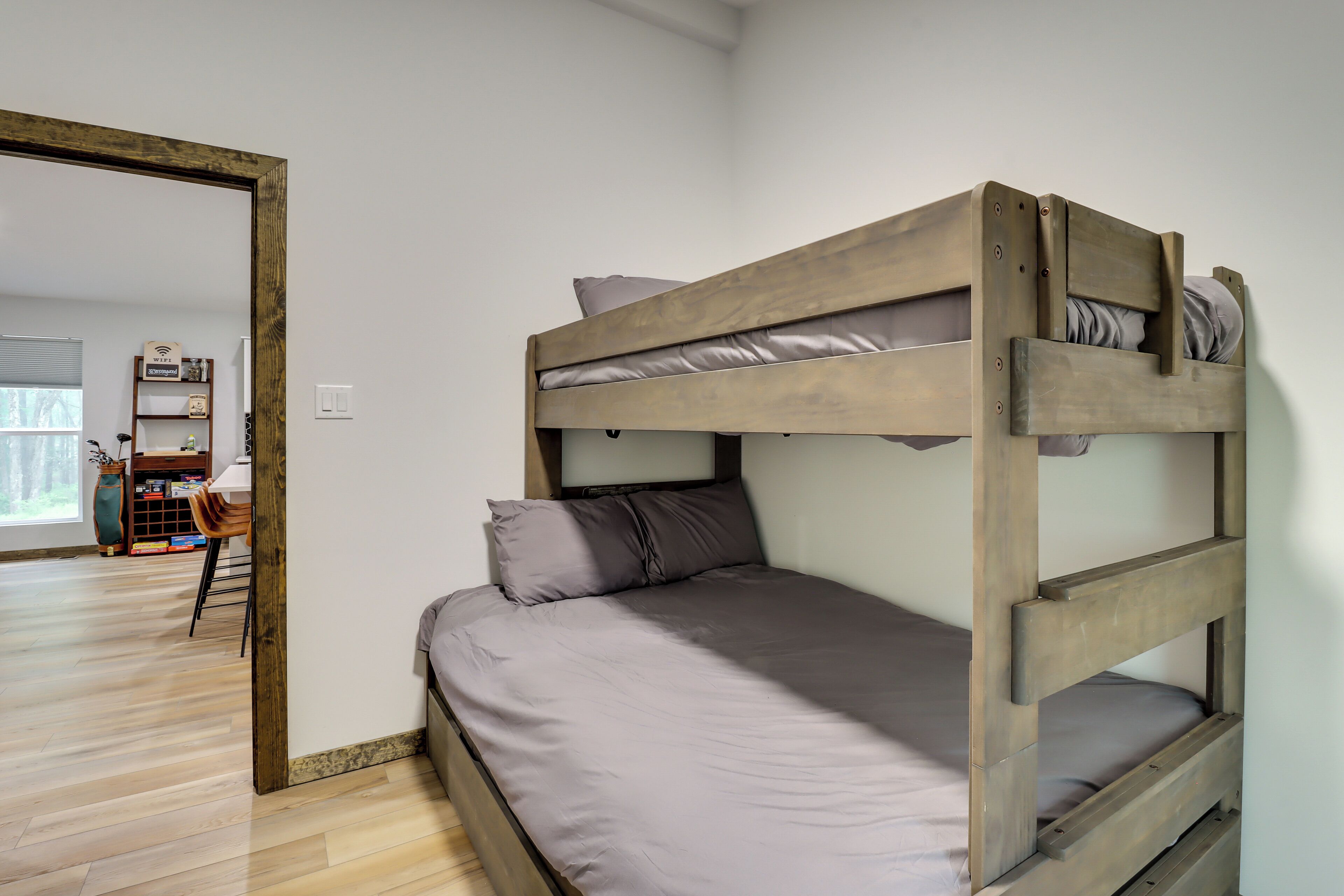 A bunk bed with a grey mattress and pillows, wooden headboard, and a wooden floor.