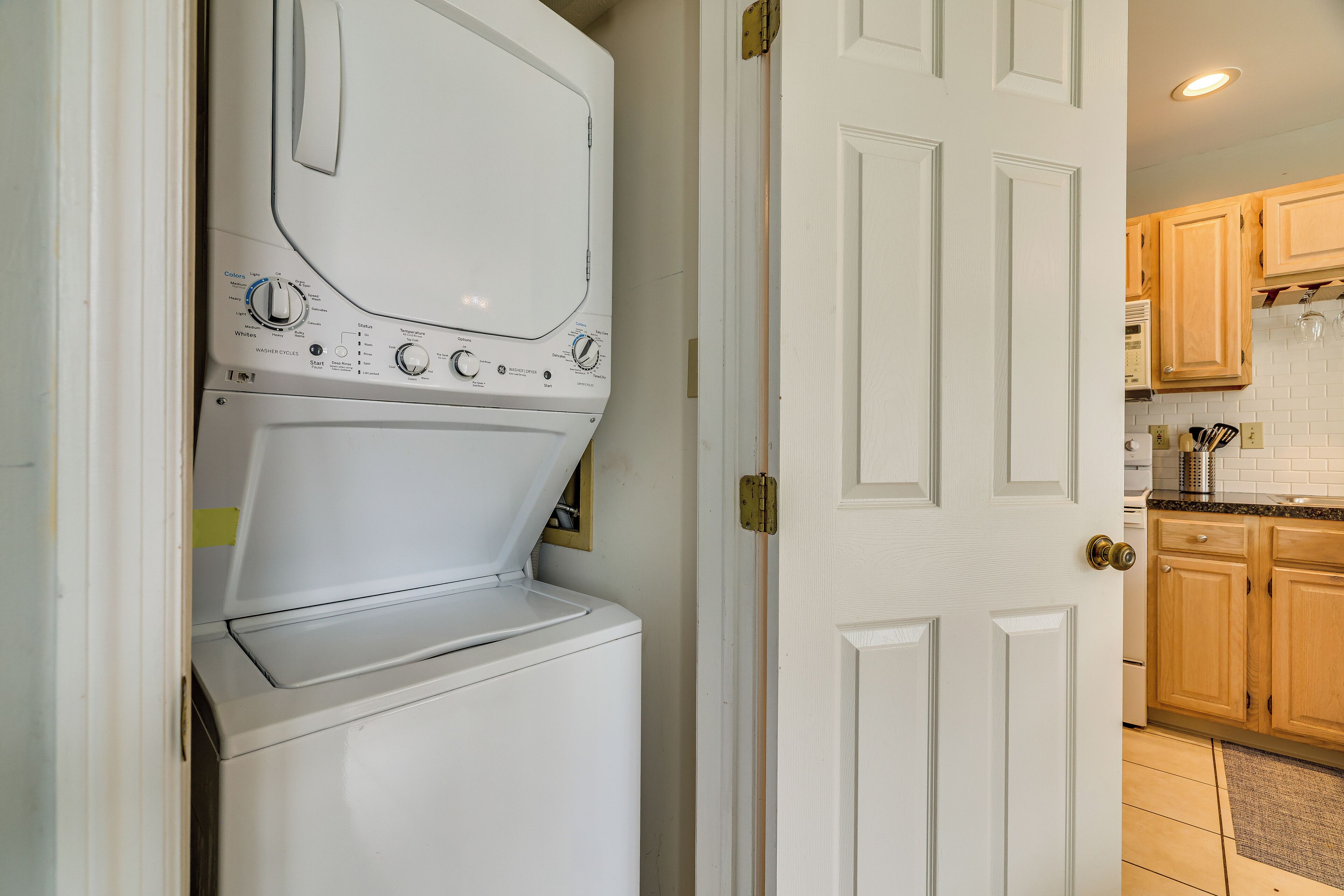 A laundry room with a front-loading washer and dryer, wooden cabinets, and a tiled backsplash in the adjacent kitchen area.