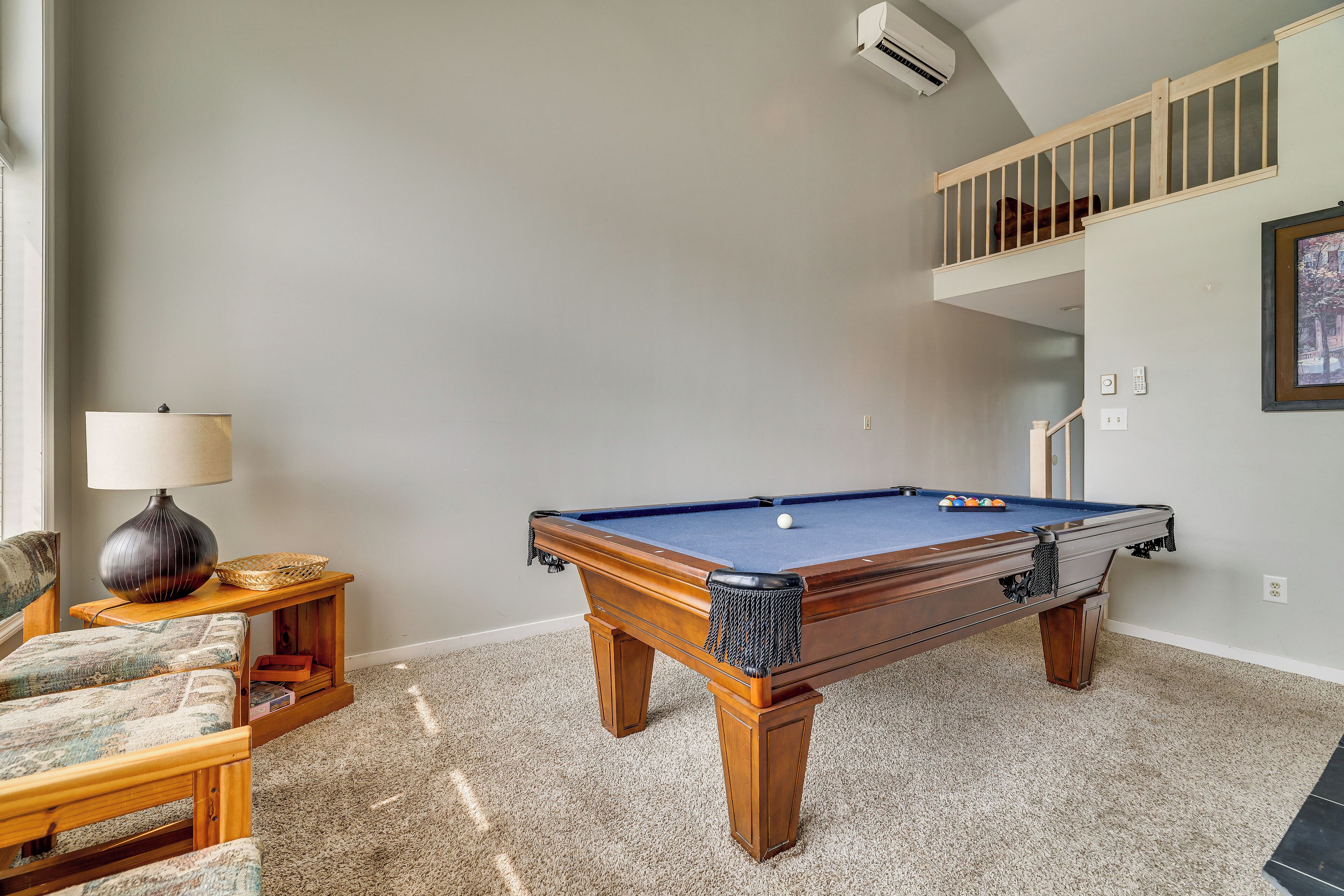 A pool table in a room with a staircase, a lamp, and a chair.