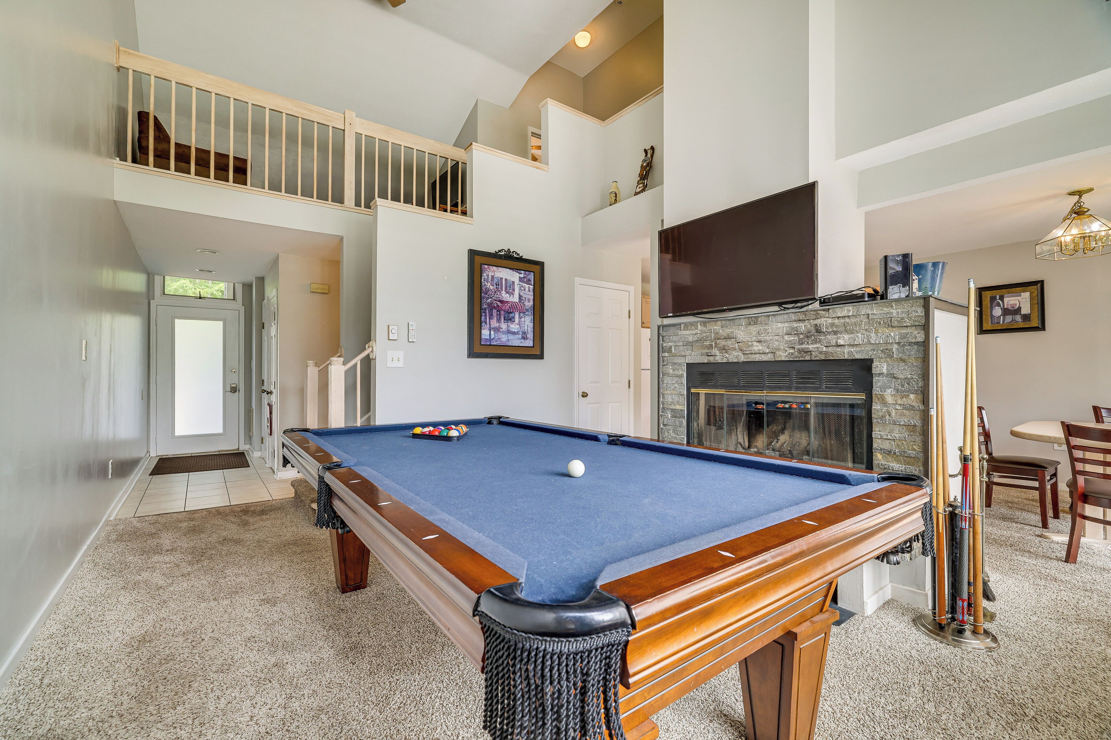 A pool table in a spacious room with a fireplace, a staircase, and a dining area.