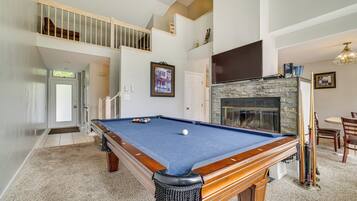 A pool table in a spacious room with a fireplace, a staircase, and a dining area.