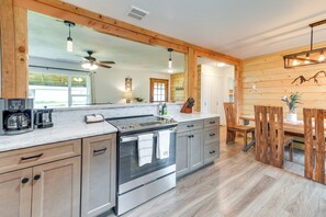 Een moderne keuken met een groot eiland, roestvrijstalen apparatuur, houten keukenkastjes en een zithoek met een houten tafel en stoelen.