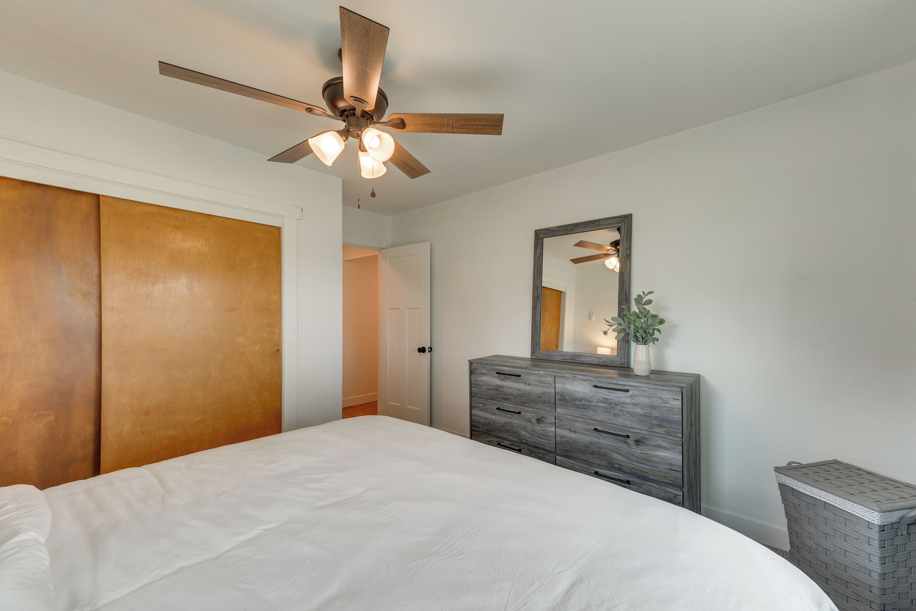 A bedroom with a bed, wooden wardrobe, ceiling fan, and a mirror on the wall.
